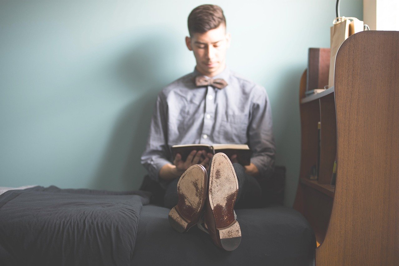 man man sitting on a bed and reading a book